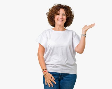 Kadın kıdemli neşeli sunulması ve kameraya bakarak avucunun ile işaret gülümseyen izole arka plan üzerinde beyaz t-shirt giyen güzel orta ager.