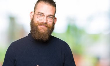 Gözlük ve balıkçı yaka kazak giyen genç sarışın adam birlikte elleri ve çapraz rahat ve neşeli gülümseyen parmak. Başarı ve iyimser