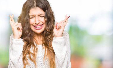 Geçiş parmakları umut ve gözler gülümseyen beyaz kazak giyen genç güzel kadın kapalı. Şans ve batıl kavramı.