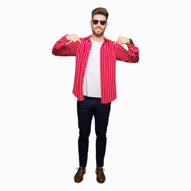 Yüzünde gülümseme ile kendinden emin görünüyorsun, kendini gururlu ve mutlu parmakları ile işaret giyen güneş gözlüğü genç yakışıklı adam.