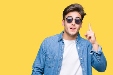 Genç yakışıklı adam başarılı fikirle izole arka plan işaret parmağı üzerinde güneş gözlüğü takıyor. Çıktıktan ve mutlu. Bir numara.