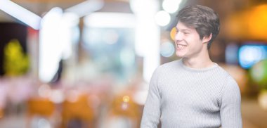 Üzerinde kış kazak giyen genç yakışıklı adam arka plan uzak tarafına gülümseme ile yüzünde, doğal ifade arıyorum izole. Kendine güvenen gülüyor.