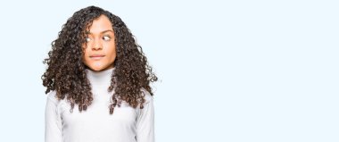 Kıvırcık saçlı görünümlü yan ve dik dik bakma uzağa düşünce gülümseyen boğazlı kazak giyen genç güzel kadın.