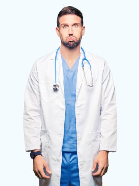 Yakışıklı Doktor komik surat ile yanakları şişirme izole arka plan üzerinde tıbbi üniforma giyen adam. Ağız ile hava, deli ifade şişirilmiş.