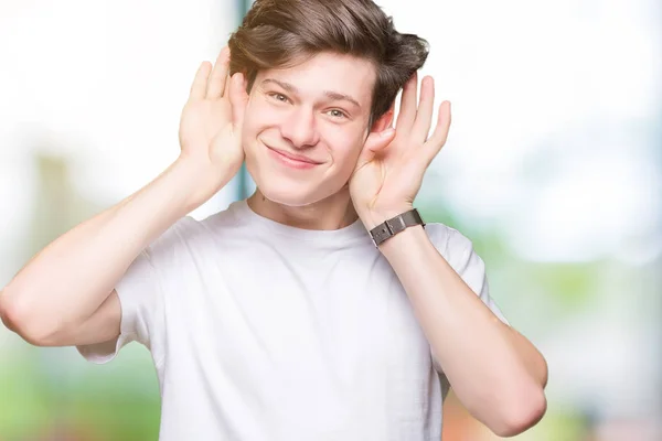 耳ジェスチャー ゴシップに興味津 の両方の手を聞くしようとすると 分離の背景にカジュアルな白い シャツを着ての若いハンサムな男 聴覚障害者 — ストック写真