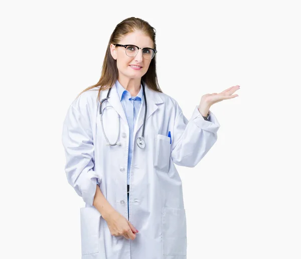 陽気な提示とカメラを見て手の手のひらで指している笑みを浮かべて分離の背景に医療のコートを着て中年中高年医師女性 — ストック写真