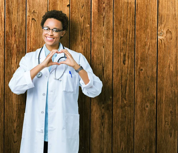年轻的非洲医生妇女穿着医疗外套在孤立的背景微笑着在爱中显示心脏符号和形状与手 浪漫的概念 — 图库照片