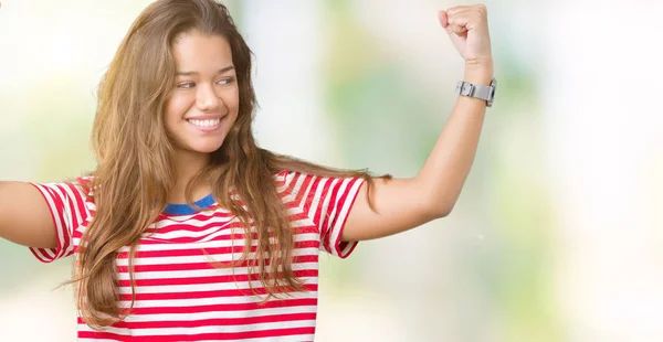 年轻美丽的黑发女人穿着条纹 T恤在孤立的背景显示手臂肌肉微笑自豪 健身理念 — 图库照片