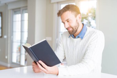 Evde kitap okuyan yakışıklı bir adam.