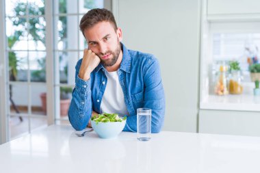 Yakışıklı adam taze sağlıklı salata düşünme seyir yeme yorgun ve sıkılmış çapraz silah depresyon sorunları ile.
