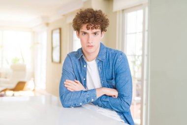 Genç yakışıklı adam giyiyor rahat denim ceket evde şüpheci ve sinir, onaylamayan ifade yüz çapraz kolları üzerinde. Negatif kişi.