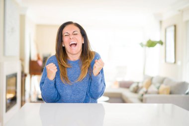 Gülümseyen ve başarı için çığlık güzel orta yaş kadın evde çok mutlu ve heyecanlı kaldırdı, silah ile kazanan jest yapıyor. Kutlama kavramı.