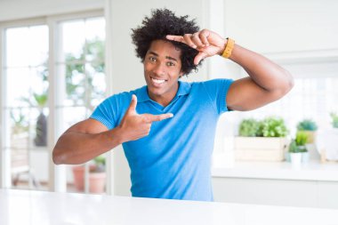 Afrika kökenli Amerikalı adam evde elleriyle yapım çerçeve ve parmakları ile mutlu yüz gülümsemeye. Yaratıcılık ve Fotoğrafçılık kavramı.