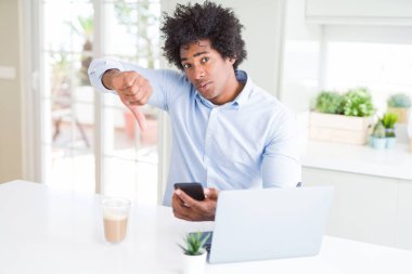 Smartphone ve dizüstü kullanarak kızgın yüzü, eksi işareti aşağı antipati başparmak ile gösterilen, ret kavramı ile Afrika kökenli Amerikalı iş adamı