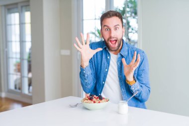 Yakışıklı adam yeme hububat evde kahvaltı için deli ve başarı için hayran kaldırdı Kollarını açarak kutluyor ve heyecanlı çığlık gözleri açık. Kazanan kavramı