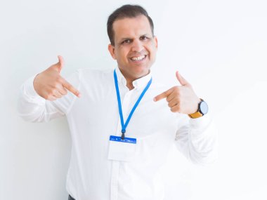 Orta yaş iş adamı yüzünde gülümseme ile kendinden emin görünüyorsun, kendini gururlu ve mutlu parmakları ile işaret beyaz arka plan üzerinde kimlik kartı takıyor.