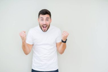 Yakışıklı delikanlı izole arka plan kutlama üzerinde rahat beyaz t-shirt giyen şaşırttı ve silah ile başarı için yükseltilmiş ve açık gözler hayrete düşürdü. Kazanan kavramı.