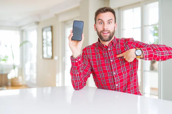 Handsome man showing smartphone screen with surprise face pointing finger to himself