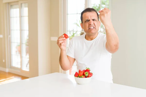 Middelaldrende Mann Som Spiser Jordbær Hjemme Irritert Frustrert Roping Med – stockfoto