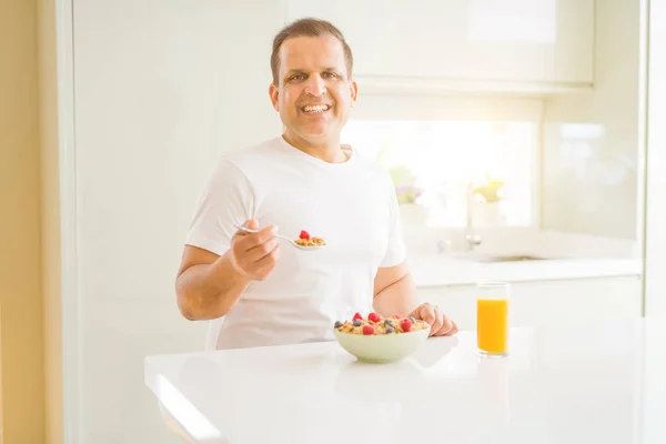 Middle age man eating strawberries at home with a happy face standing and smiling with a confident smile showing teeth