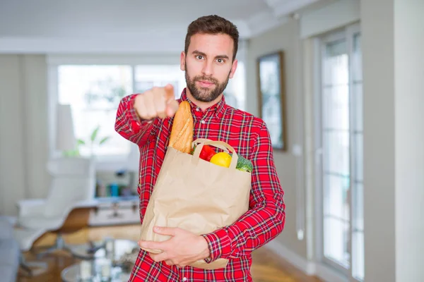 Handsome man holding groceries bag pointing with finger to the camera and to you, hand sign, positive and confident gesture from the front