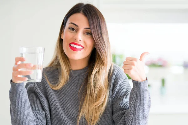 Young Beautiful Woman Drinking Glass Water Home Pointing Showing Thumb — Stock Photo, Image