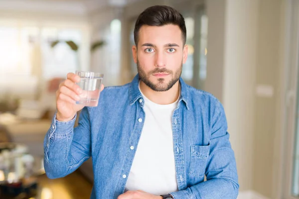 スマートの顔は深刻な思考に自信を持って式に家庭での水のガラスを飲む若いハンサムな男 — ストック写真