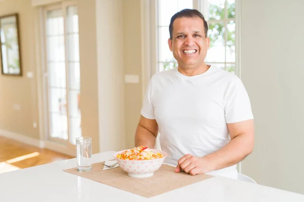 Middle age man eating rice at home with a happy and cool smile on face. Lucky person.