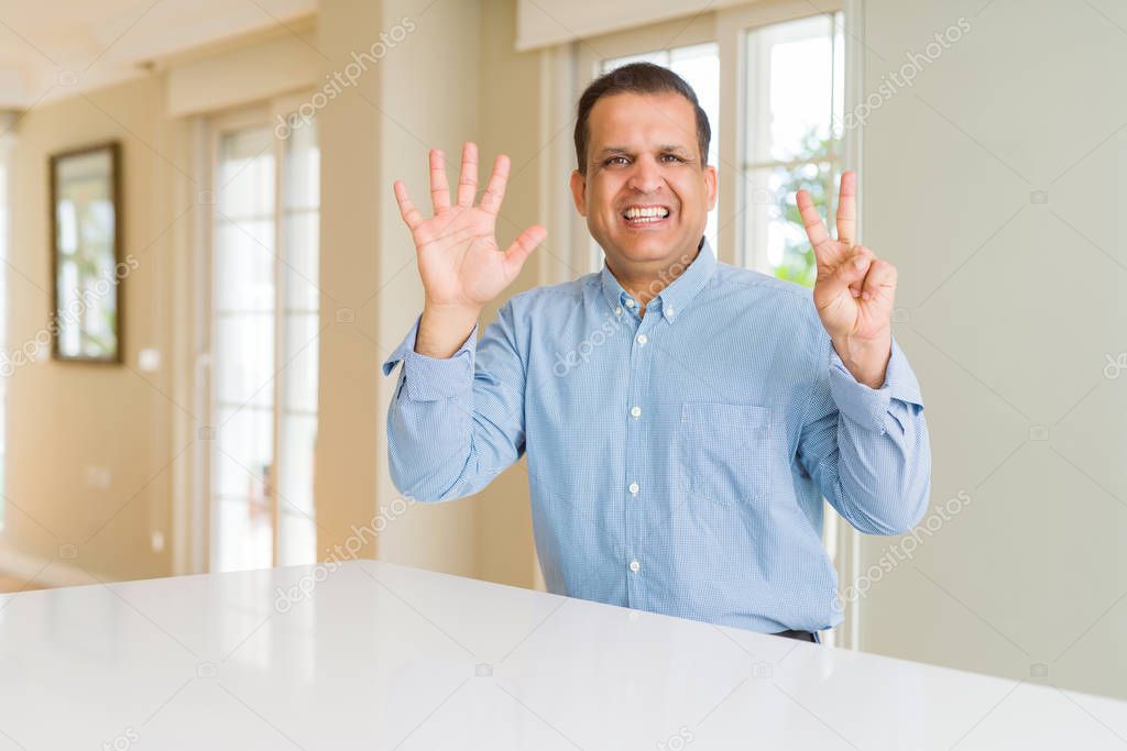 Middle age man sitting at home showing and pointing up with fingers number seven while smiling confident and happy.
