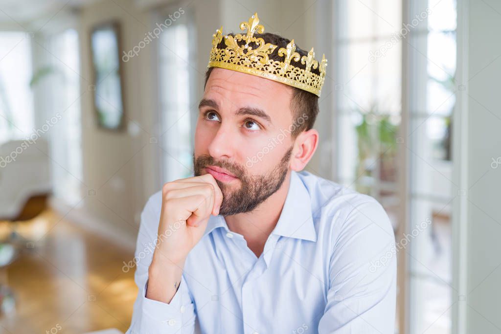 Handsome business man wearing golden crown as a king or prince with hand on chin thinking about question, pensive expression. Smiling with thoughtful face. Doubt concept.