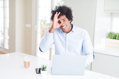 Afrika kökenli Amerikalı iş adamı mutlu yüz el parmaklarının arasından seyir göz üzerinde ok işaretiyle yapıyor gülümseyen ile dizüstü bilgisayar kullanarak çalışma