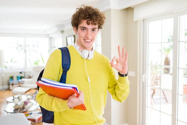 年轻的学生男子戴着耳机和背包拿着笔记本做确定的标志与手指 优秀的符号 — 图库照片