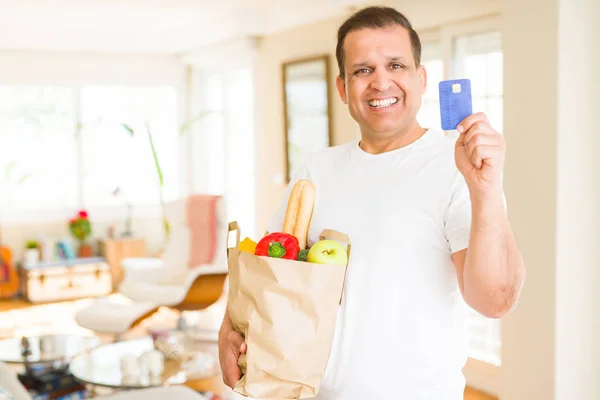 Średnim wieku człowiek trzyma worek produkty spożywcze i wyświetlone karty kredytowej — Zdjęcie stockowe