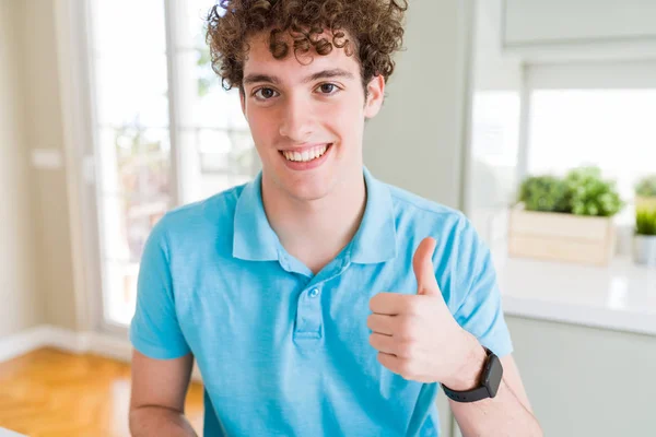 カジュアルなブルー シャツを着て家で若いハンサムな男は 幸せの親指を手でジェスチャーをやっています 成功を示すと カメラを見て式を承認します — ストック写真