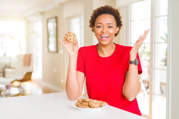 Young african american woman eating chocolate chips cookies very happy and excited, winner expression celebrating victory screaming with big smile and raised hands
