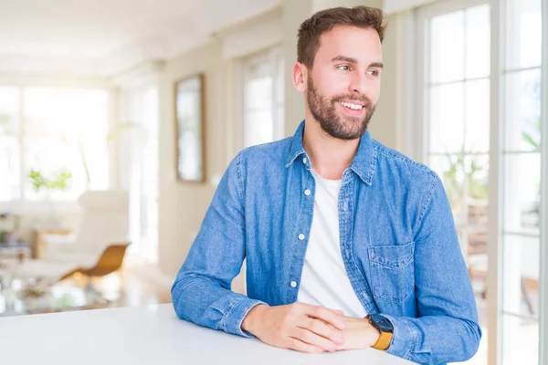 Handsome man at home looking away to side with smile on face, natural expression. Laughing confident.