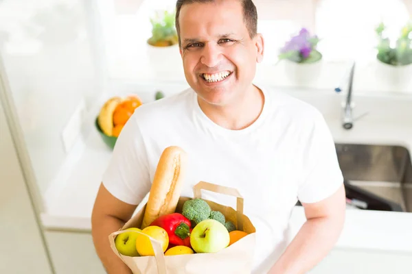 Middle age man holding grocieries bag full of vegetables at home — Stock Photo, Image