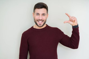 Yakışıklı genç gülümseyen izole arka plan ve süre seyir ve kamera boyutu işaret parmaklarıyla yapıyor el ile kendinden emin eller üzerinde bir kazak giyiyor. Ölçü kavramı.