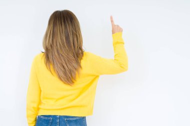 Üzerinde izole sarı kazak giyen güzel orta yaş kadın arka plan geriye doğru arkasında parmak eliyle işaret Posing