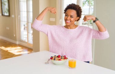 Sabahları sağlıklı kahvaltı evde gururlu gülümseyen gösteren kol kasları olan genç Afro-Amerikan kadın. Fitness kavramı.