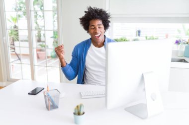 Gülümseyen ve başarı için çığlık çok mutlu ve heyecanlı kaldırdı, silah ile kazanan jest yapıyor bilgisayarla çalışma Afro-Amerikan bir adam. Kutlama kavramı.