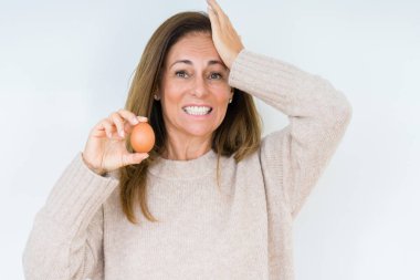 Taze Yumurta kafa üzerinde el ile vurguladı izole arka plan üzerinde tutan orta yaş kadın şok utanç ve sürpriz suratla, öfkeli ve sinirli. Korku ve hata için üzgün.