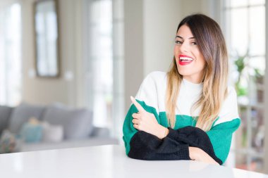 Genç güzel kadın giyiyor kış kazak ve neşeli bir gülümseme yüzünü elimle işaret ile ev yan yüzünde mutlu ve doğal ifade ile kadar parmak