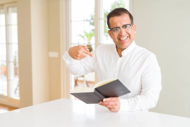 Orta yaş erkek evde kitap okurken sürpriz yüz işaret parmağı kendine gözlük