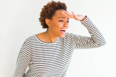 Giyen genç güzel Afrikalı-Amerikalı kadın Kazak çok mutlu ve gülümseyen uzakta el ile üzerine kafa seyir beyaz arka plan üzerinde çizgili. Arama kavramı.