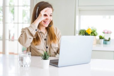 Laptop ile çalışma ve ok işareti ile el parmaklarının arasından seyir göze yapıyor gülümseyen mutlu yüz ile headseat giyen güzel genç operatör kadın