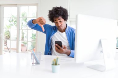 Afrika kökenli Amerikalı adam akıllı telefon ve bilgisayar kullanarak kızgın yüzü, eksi işareti aşağı antipati başparmak ile gösterilen, ret kavramı ile çalışma