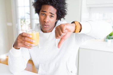 Holding ve kızgın yüzü, eksi işareti aşağı antipati başparmak ile gösterilen, ret kavramı ile portakal suyu bardak içme Afrikalı-Amerikalı adam