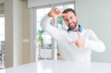 Elle yapma çerçeve ve parmakları ile mutlu yüz gülümseyen rahat kazak giyen yakışıklı adam. Yaratıcılık ve Fotoğrafçılık kavramı.