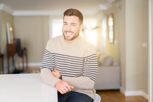 Young handsome man wearing a sweater at home looking away to side with smile on face, natural expression. Laughing confident.
